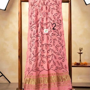 May include: A light pink fabric drape featuring a dark maroon embroidered leaf pattern and a wide metallic gold border at the bottom. The fabric has a crinkled texture and displays the number 2 in black print near the center of the material.