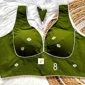 May include: Olive green sleeveless top with white trim and floral embroidery. The top features a scoop neckline and a small patch with a cartoon image. The number "8" is printed on the front.