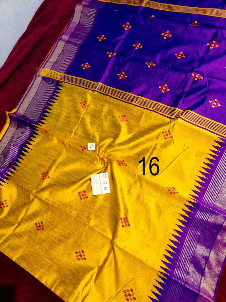 May include: A colourful textile in yellow and purple. The fabric has a repeating pattern of small, colourful floral designs. The number "16" is visible on the yellow section. The edges are trimmed with a decorative border.
