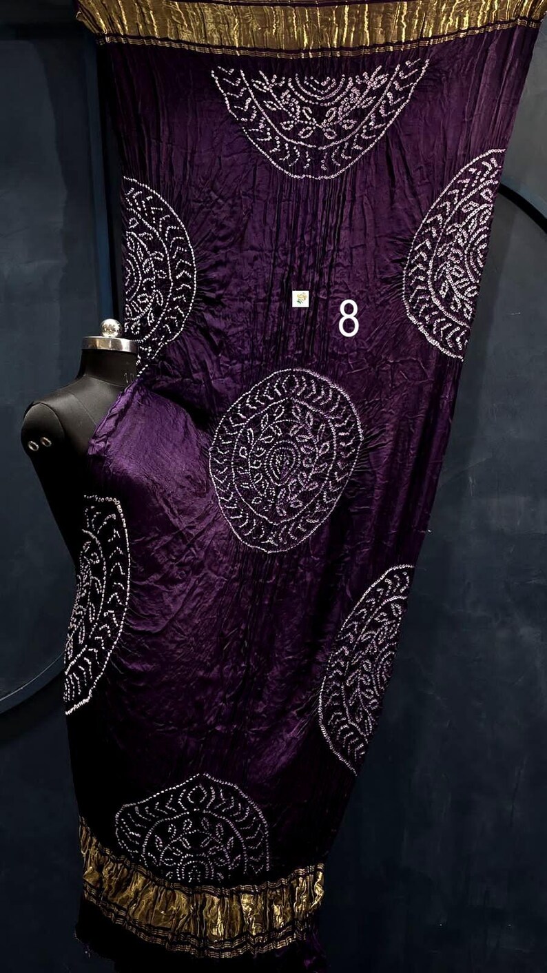 May include: A deep purple fabric wrap featuring white circular mandala-style patterns and a metallic gold border at the top and bottom edges. The fabric has a crinkled texture and displays the number 8 in white text on the front surface.