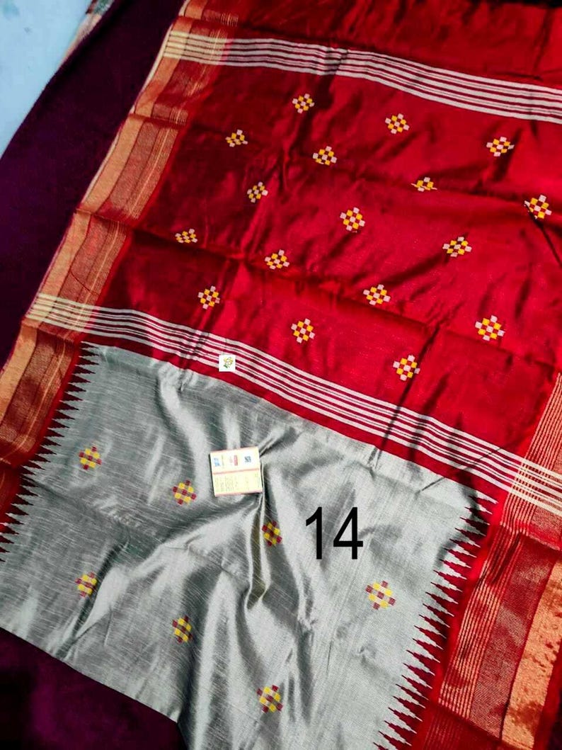 May include: A red and grey sari with a decorative pattern. The red section has small, square yellow and red designs. The grey section has the number 14 printed on it. The sari has a gold border.