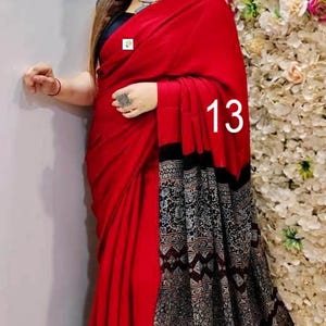 Puede incluir: Un sari de color rojo vibrante con un cuerpo rojo s&oacute;lido y un pallu negro en contraste adornado con intrincados patrones geom&eacute;tricos y florales en blanco y gris. La tela se drapea elegantemente, mostrando una combinaci&oacute;n audaz y el n&uacute;mero 13.