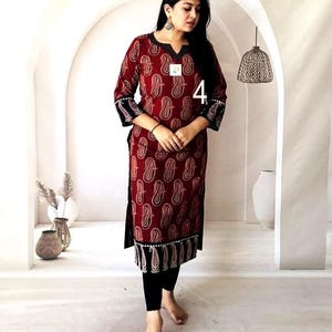 Puede incluir: Una kurta burdeos con un estampado de cachemira, pu&ntilde;os negros y un dobladillo negro. La kurta se usa con leggings negros. El n&uacute;mero "4" es visible en la kurta. El atuendo lo lleva una persona.