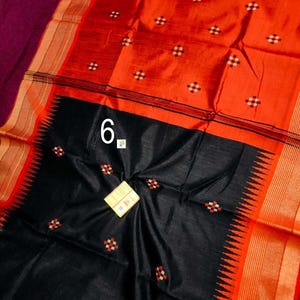 May include: A vibrant orange and black sari with a geometric pattern. The sari features a black lower section with a decorative edge and the number "6" in white. The sari has a maroon border and gold accents.