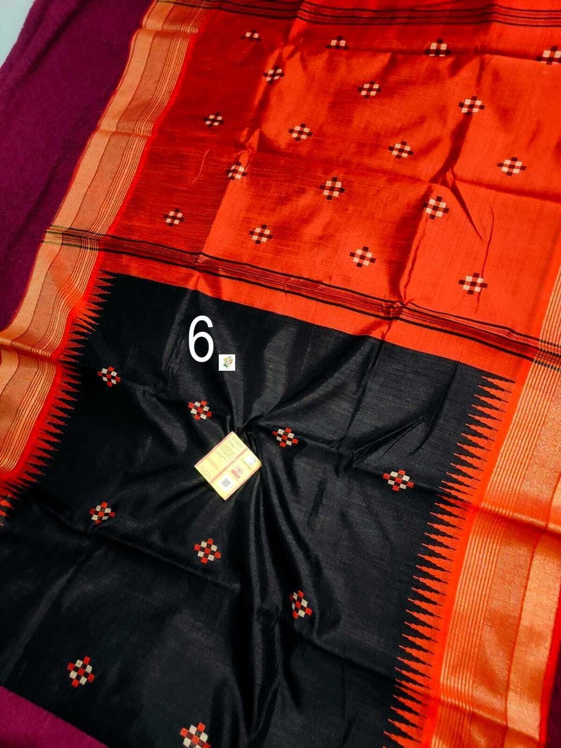 May include: A vibrant orange and black sari with a geometric pattern. The sari features a black lower section with a decorative edge and the number "6" in white. The sari has a maroon border and gold accents.