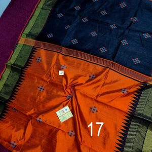 May include: A vibrant orange and navy blue saree with a geometric pattern. The saree features a contrasting border with black and gold accents. The number 17 is visible on the orange portion of the saree.