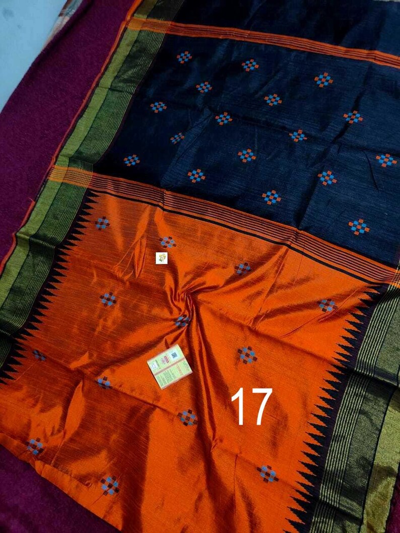 May include: A vibrant orange and navy blue saree with a geometric pattern. The saree features a contrasting border with black and gold accents. The number 17 is visible on the orange portion of the saree.