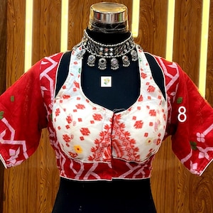 May include: A red and white patterned blouse with short sleeves, displayed on a mannequin. The blouse features a white bodice with red floral designs and red sleeves with a geometric pattern. A silver necklace is around the mannequin's neck. The number "8" is visible on the side.