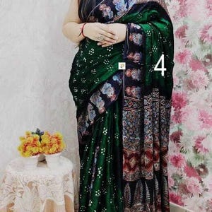 May include: A dark green and black saree featuring a white dotted bandhani pattern on the main body, complemented by a wide border with intricate multi-colored floral and geometric motifs. The number 4 is visible on the fabric.