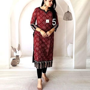 Puede incluir: Una t&uacute;nica larga roja con un patr&oacute;n circular repetitivo y detalles en negro. La t&uacute;nica tiene mangas tres cuartos y un borde negro en el dobladillo. La modelo lleva leggings negros. El n&uacute;mero "5" es visible en la t&uacute;nica.