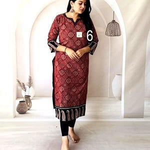 Puede incluir: Una t&uacute;nica larga roja con un estampado de cachemira, ribetes negros y mangas tres cuartos. La t&uacute;nica se combina con leggings negros. El n&uacute;mero "6" es visible en la t&uacute;nica. El atuendo es adecuado para ropa casual.