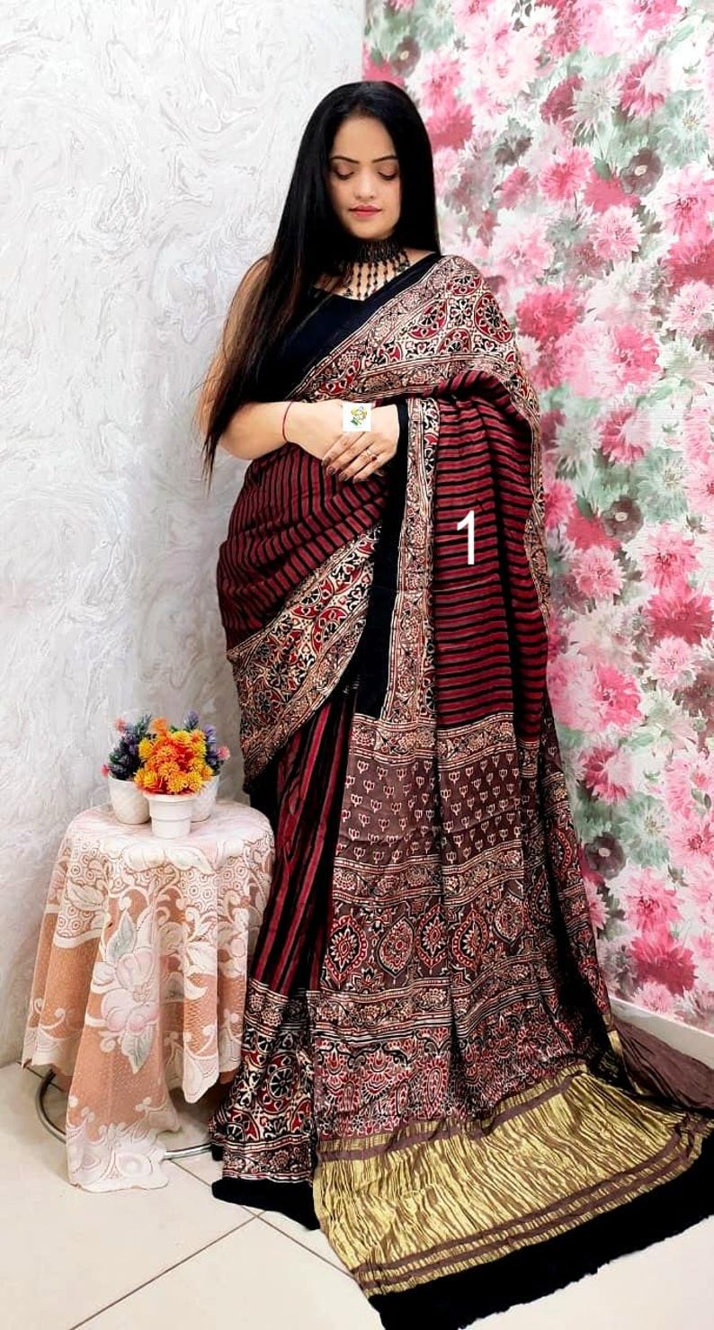 May include: A saree featuring a black bodice and a skirt with dark red and black horizontal stripes. The fabric is adorned with intricate block-printed patterns in black, red, and white, finished with a metallic gold pleated border at the hem.