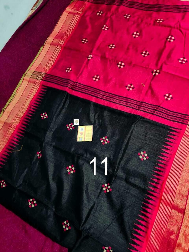 May include: A striking red and black textile with a geometric design. The fabric displays a vivid red field adorned with small white and red square patterns. A black section at the bottom has the number "11" printed on it. The edges are trimmed with gold and black stripes.