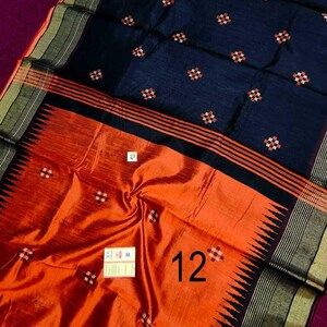 May include: A dark blue and orange saree with a detailed design. The saree features a dark blue upper portion with small, repeating floral patterns in white and orange. The lower portion is orange with a repeating pattern and the number "12".