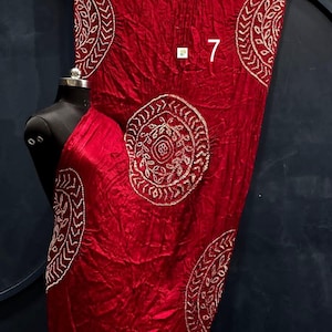 May include: A deep red fabric drape featuring a repeating circular pattern with white embroidered details and a gold border. The fabric has a crinkled texture and displays the number 7 in white text near the centre of the material.
