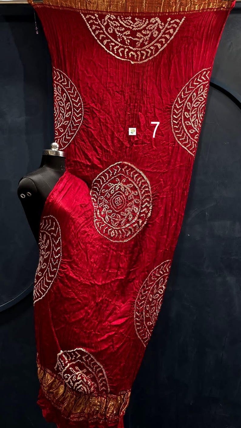 May include: A deep red fabric drape featuring a repeating circular pattern with white embroidered details and a gold border. The fabric has a crinkled texture and displays the number 7 in white text near the centre of the material.