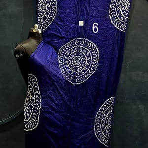 May include: A deep blue fabric drape featuring large white circular patterns with intricate dot details. The fabric has a metallic gold border at the top and bottom edges. A small white square tag with the number 6 is visible on the fabric.