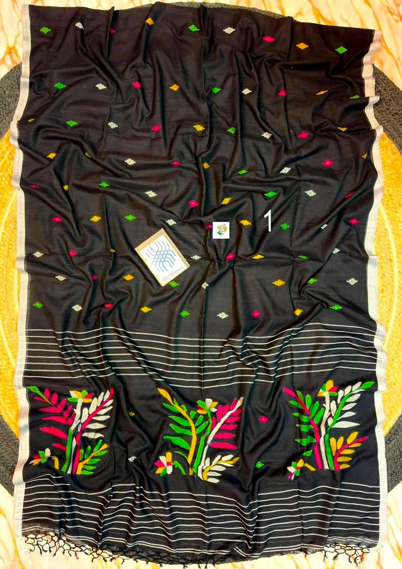 May include: A black textile featuring a pattern of small, scattered diamond-shaped motifs in yellow, green, and pink. The lower section displays horizontal white stripes and three large, colorful floral designs in pink, green, and yellow.