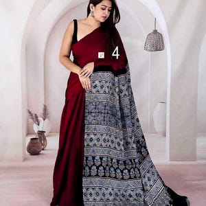Puede incluir: Un sari granate que presenta un drapeado de color s&oacute;lido combinado con un pallu en contraste que muestra un complejo patr&oacute;n geom&eacute;trico y floral en tonos azules, blancos y negros. La prenda incluye el n&uacute;mero 4 impreso en la tela.