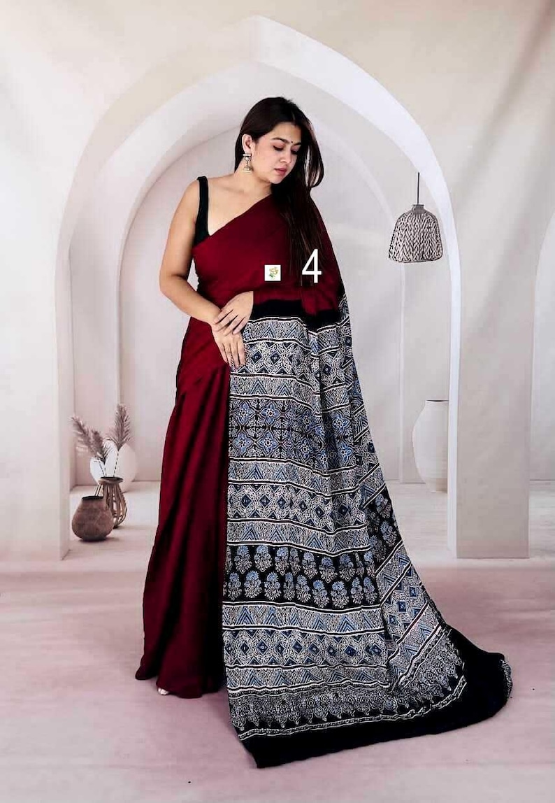 Puede incluir: Un sari granate que presenta un drapeado de color s&oacute;lido combinado con un pallu en contraste que muestra un complejo patr&oacute;n geom&eacute;trico y floral en tonos azules, blancos y negros. La prenda incluye el n&uacute;mero 4 impreso en la tela.