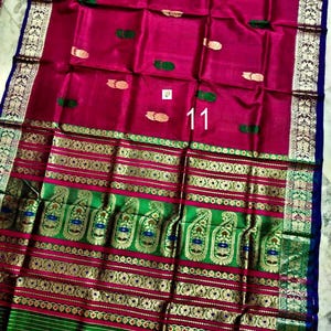 May include: A magenta saree featuring a wide green border with gold zari paisley and floral patterns. The main fabric displays small gold and green motifs scattered across the surface. The number 11 is printed in white on the center of the fabric.