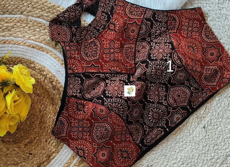 Puede incluir: Una blusa con estampado rojo y negro con un escote de ojo de cerradura y un ribete negro. La blusa tiene un dise&ntilde;o tradicional indio.