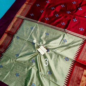 May include: A two-toned textile with a red top and a light green bottom. The red section features small, embroidered floral patterns in blue, red, and white. The light green section also has similar floral patterns. The number "3" is visible.