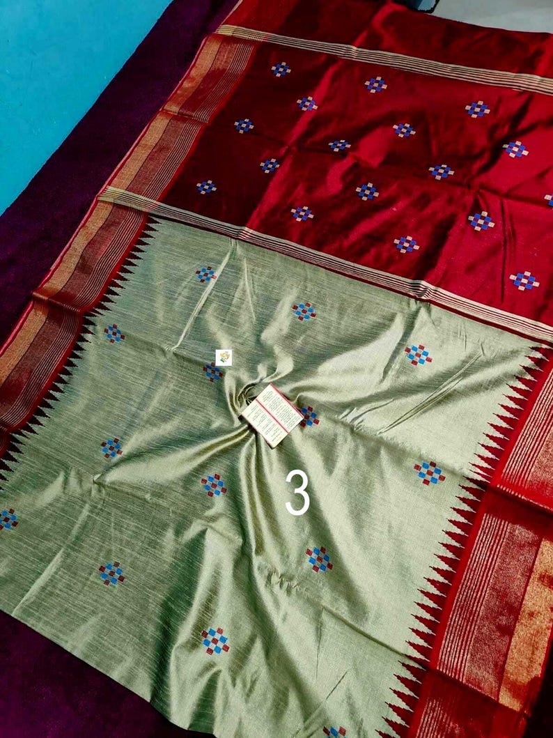 May include: A two-toned textile with a red top and a light green bottom. The red section features small, embroidered floral patterns in blue, red, and white. The light green section also has similar floral patterns. The number "3" is visible.