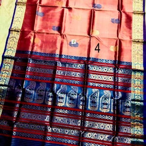 May include: A peach-colored saree featuring a large number 4 in the center, adorned with small blue and gold floral motifs. The wide border displays intricate blue and gold patterns, including paisley designs and horizontal stripes throughout.