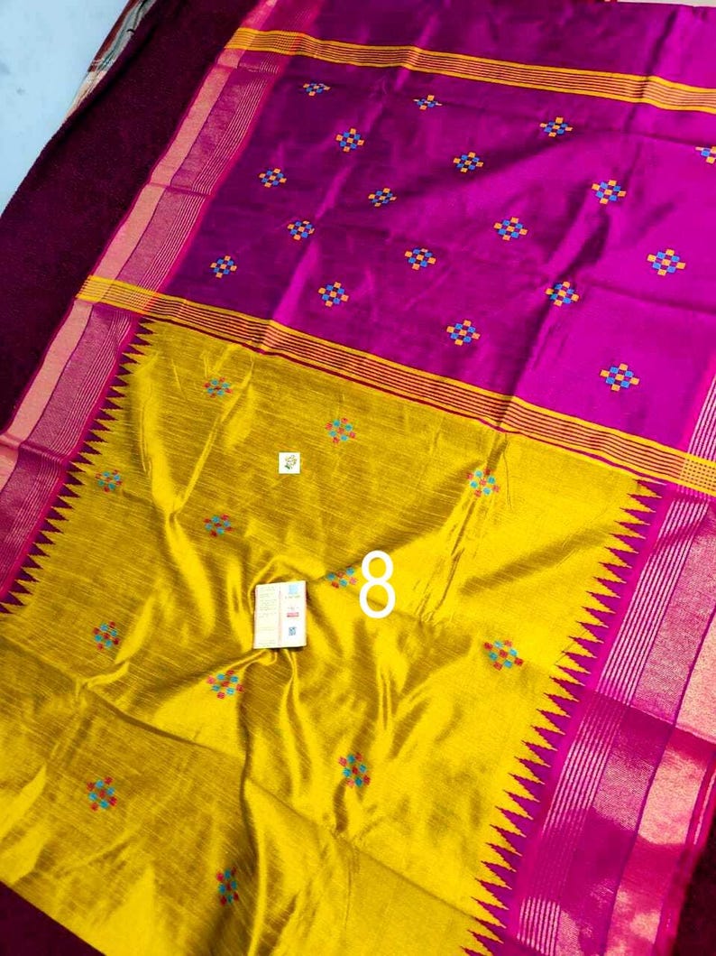 May include: A colourful textile in magenta and yellow. The fabric is decorated with small, multi-coloured floral embroidery. The design includes a yellow border with a zigzag pattern and a magenta border with stripes. Likely a saree or similar garment.