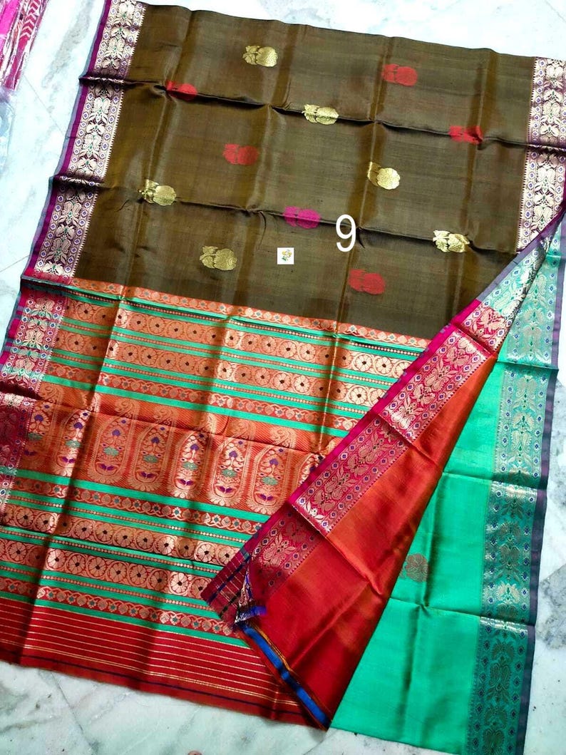 May include: A brown silk saree featuring gold and red floral motifs across the main body. The wide border displays horizontal stripes in green, orange, and red with intricate gold zari patterns. The number 9 is printed in white on the fabric.