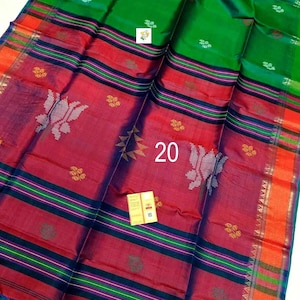 Puede incluir: Un sari de color verde vibrante y rojo intenso que presenta el n&uacute;mero 20 en el centro. La tela muestra intrincados patrones tejidos, incluyendo peque&ntilde;os motivos florales y formas estilizadas, con rayas horizontales y un borde naranja brillante.