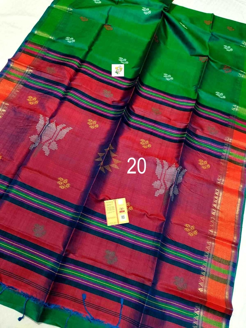 Puede incluir: Un sari de color verde vibrante y rojo intenso que presenta el n&uacute;mero 20 en el centro. La tela muestra intrincados patrones tejidos, incluyendo peque&ntilde;os motivos florales y formas estilizadas, con rayas horizontales y un borde naranja brillante.