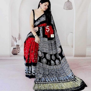 May include: A black and red saree featuring a block-printed pattern with white floral motifs. The garment includes a solid black sleeveless blouse, a red section with white dots, and a wide black border with intricate white patterns and a gold hem.