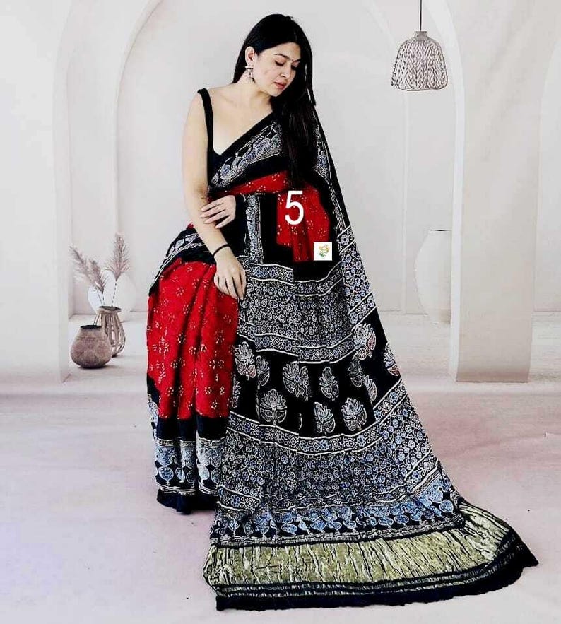 May include: A black and red saree featuring a block-printed pattern with white floral motifs. The garment includes a solid black sleeveless blouse, a red section with white dots, and a wide black border with intricate white patterns and a gold hem.