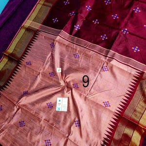 May include: A maroon and peach-coloured silk sari with a geometric pattern of small blue and purple squares. The sari has a decorative border with gold accents and a zigzag edge. The number "9" is visible on the sari.