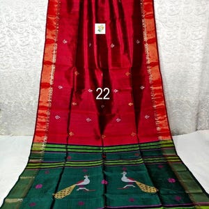 Puede incluir: Un sari de color rojo intenso con un borde ancho de color rojo vibrante y detalles met&aacute;licos dorados. La secci&oacute;n inferior es un panel verde oscuro decorado con motivos de pavos reales en blanco y oro, con rayas horizontales negras y verdes.