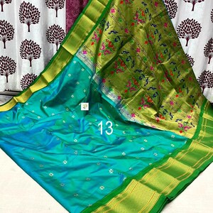 Op de afbeelding: Een turquoise sari met kleine zilveren bloemmotieven over het hele lichaam, gecombineerd met een brede olijfgroene rand en een pallu versierd met ingewikkelde pauwen- en bloempatronen in roze, groen en blauw, gemarkeerd met het nummer 13.