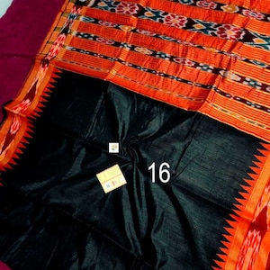 May include: A vibrant textile featuring a black base with an orange and patterned top section. The orange section has horizontal stripes with intricate designs in blue, white, and black. The edge has a red and orange zigzag pattern. The number "16" is visible.