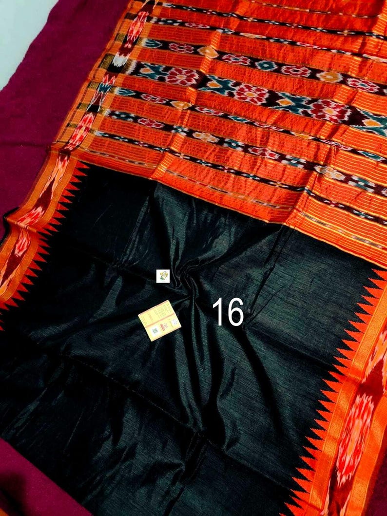 May include: A vibrant textile featuring a black base with an orange and patterned top section. The orange section has horizontal stripes with intricate designs in blue, white, and black. The edge has a red and orange zigzag pattern. The number "16" is visible.