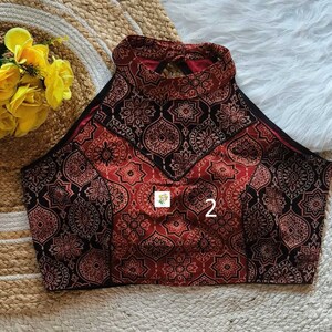 Puede incluir: Un top halter de color rojo y negro con estampado y un escote en la espalda en forma de ojo de cerradura. El top tiene un escote alto y una silueta ajustada.