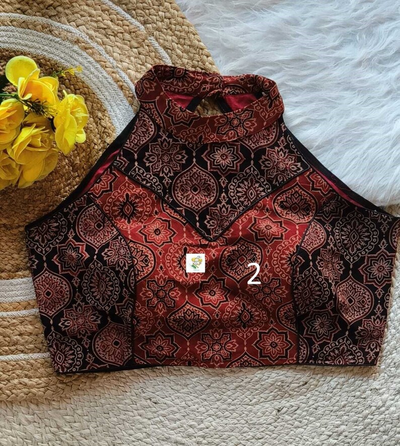 Puede incluir: Un top halter de color rojo y negro con estampado y un escote en la espalda en forma de ojo de cerradura. El top tiene un escote alto y una silueta ajustada.