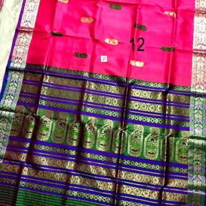 May include: A vibrant pink saree featuring small gold and green motifs scattered across the fabric. The wide border displays intricate purple and green bands with detailed gold zari paisley patterns and floral designs, finished with a silver edge.