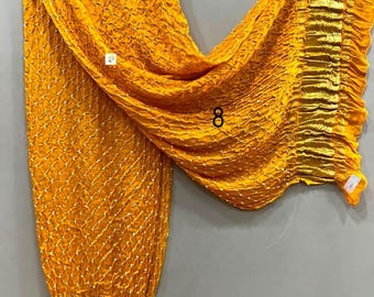 May include: A bright yellow dupatta featuring a textured, crinkled fabric with a repeating white dotted pattern across the surface. The garment includes a wide, metallic gold pleated border along the edges and is displayed on a wooden hanger.