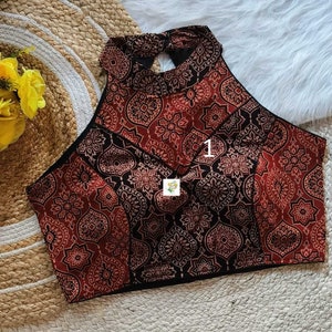 Puede incluir: Un top halter de patr&oacute;n rojo y negro con un corte de ojo de cerradura en la espalda. El top tiene un escote alto y una silueta ajustada.