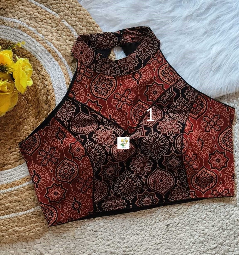 Puede incluir: Un top halter de patr&oacute;n rojo y negro con un corte de ojo de cerradura en la espalda. El top tiene un escote alto y una silueta ajustada.