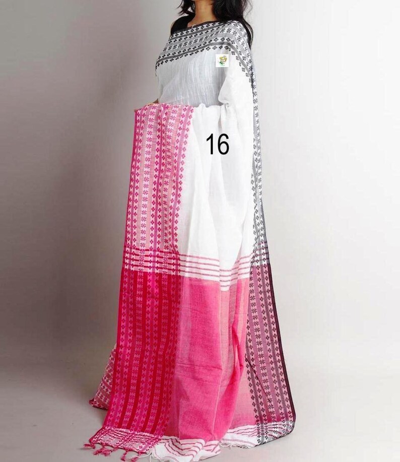 K&ouml;nnte beinhalten: Wei&szlig;-rosa Sari mit geometrischem Muster und der Zahl 16. Der Sari hat eine wei&szlig;e Basis mit einem rosa Rand und Akzenten. Der Rand weist ein sich wiederholendes geometrisches Design in Rosa und Wei&szlig; auf.