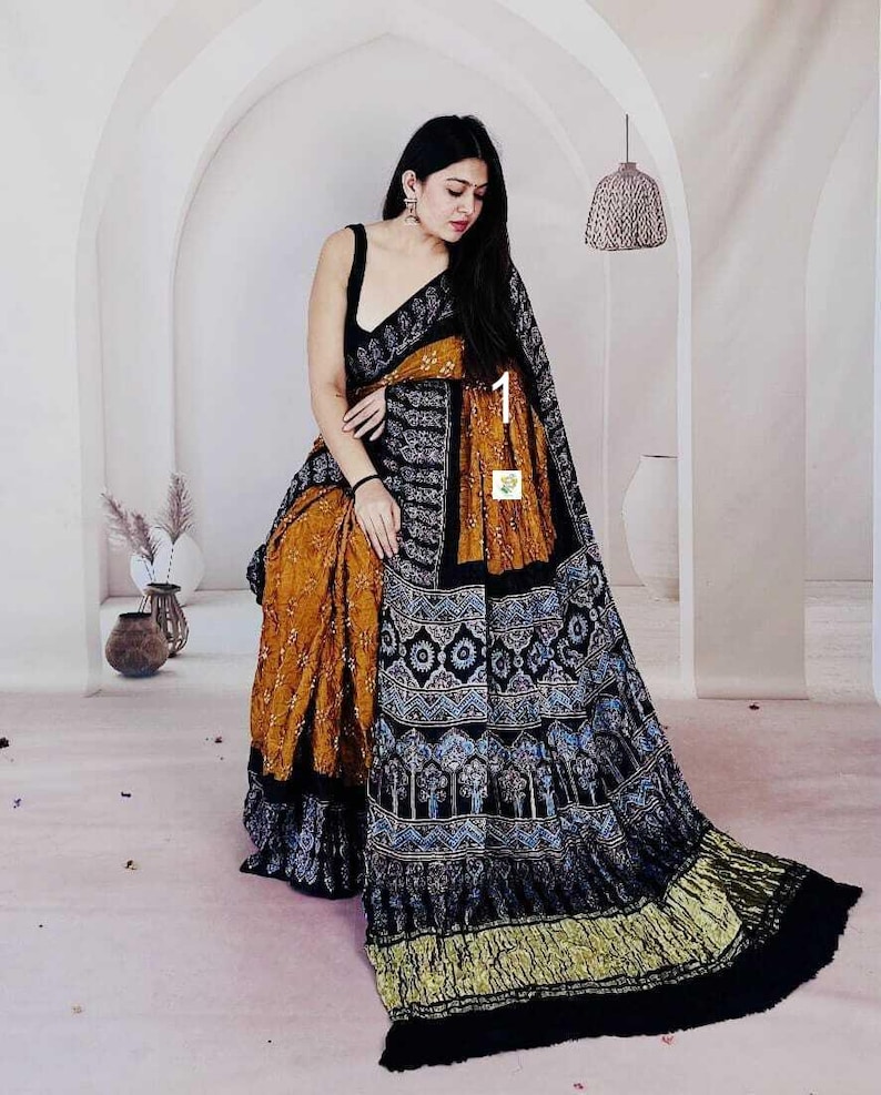 May include: A saree featuring a mustard yellow base with a black border and pallu. The fabric displays intricate black and white geometric patterns, floral motifs, and tree designs. The garment includes a sleeveless black blouse with a scoop neckline.