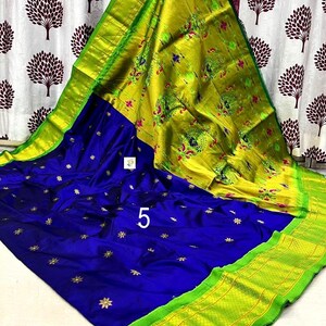 Op de afbeelding: Een levendige blauwe sari met kleine gouden stervormige motieven over het hoofdgedeelte. De pallu is fel limoengroen met ingeweven pauwenpatronen in roze en blauw. Een brede limoengroene rand met een geometrisch rasterpatroon omlijst het geheel.