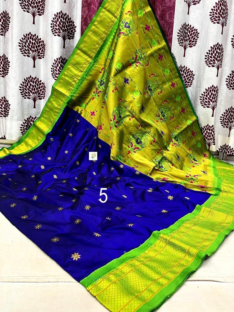 Op de afbeelding: Een levendige blauwe sari met kleine gouden stervormige motieven over het hoofdgedeelte. De pallu is fel limoengroen met ingeweven pauwenpatronen in roze en blauw. Een brede limoengroene rand met een geometrisch rasterpatroon omlijst het geheel.